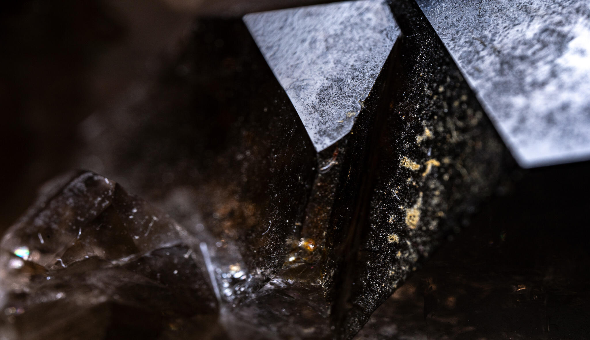 Macro photograph of a dark mineral cluster, sharp facets catching light with silver edges and golden specks in the crevices.